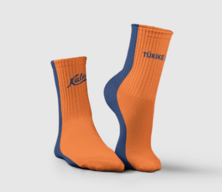 Pildil on spordisokid, mille üks külg on oranž ja teine tumesinine. Lisaks on sokkide Kalevi logo ja slogan "tükike head"